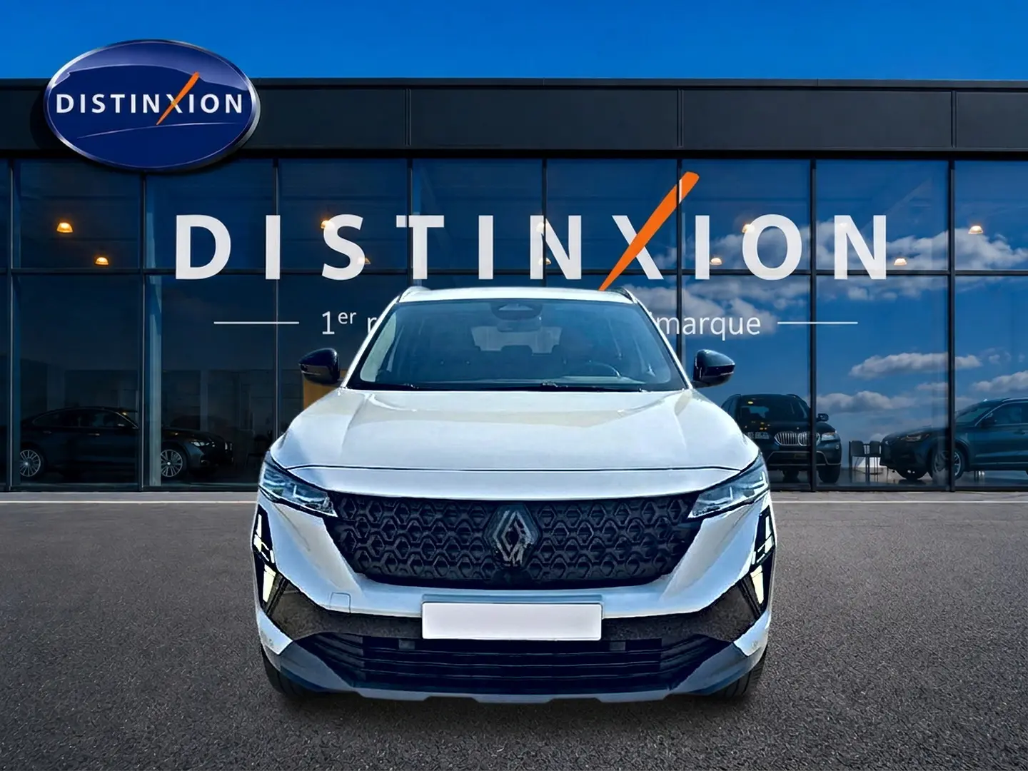 Renault Austral blanc nacré vu de face, avec calandre noire et logo Renault proéminent devant un showroom Distinxion.
