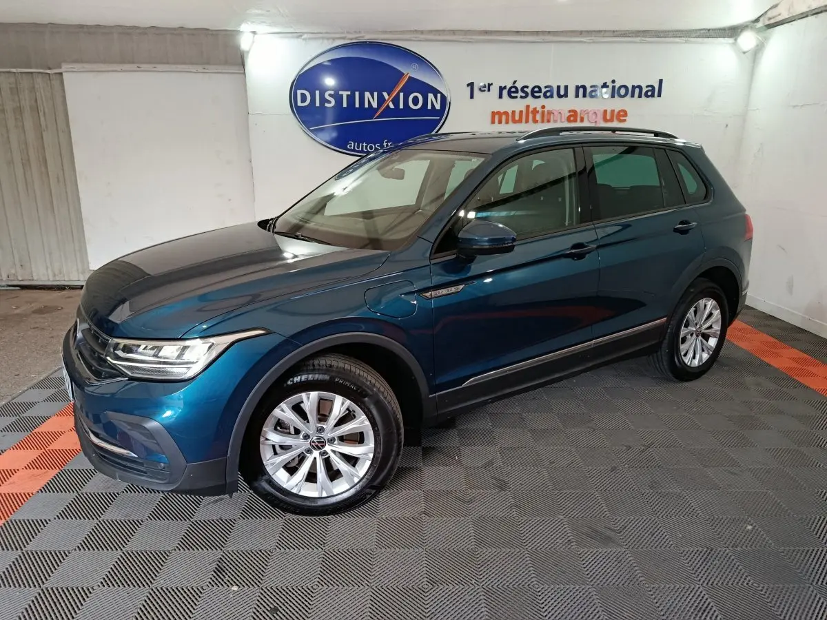 Volkswagen Tiguan bleu en 3/4 avant droit, SUV hybride rechargeable avec jantes alliage et toit noir.