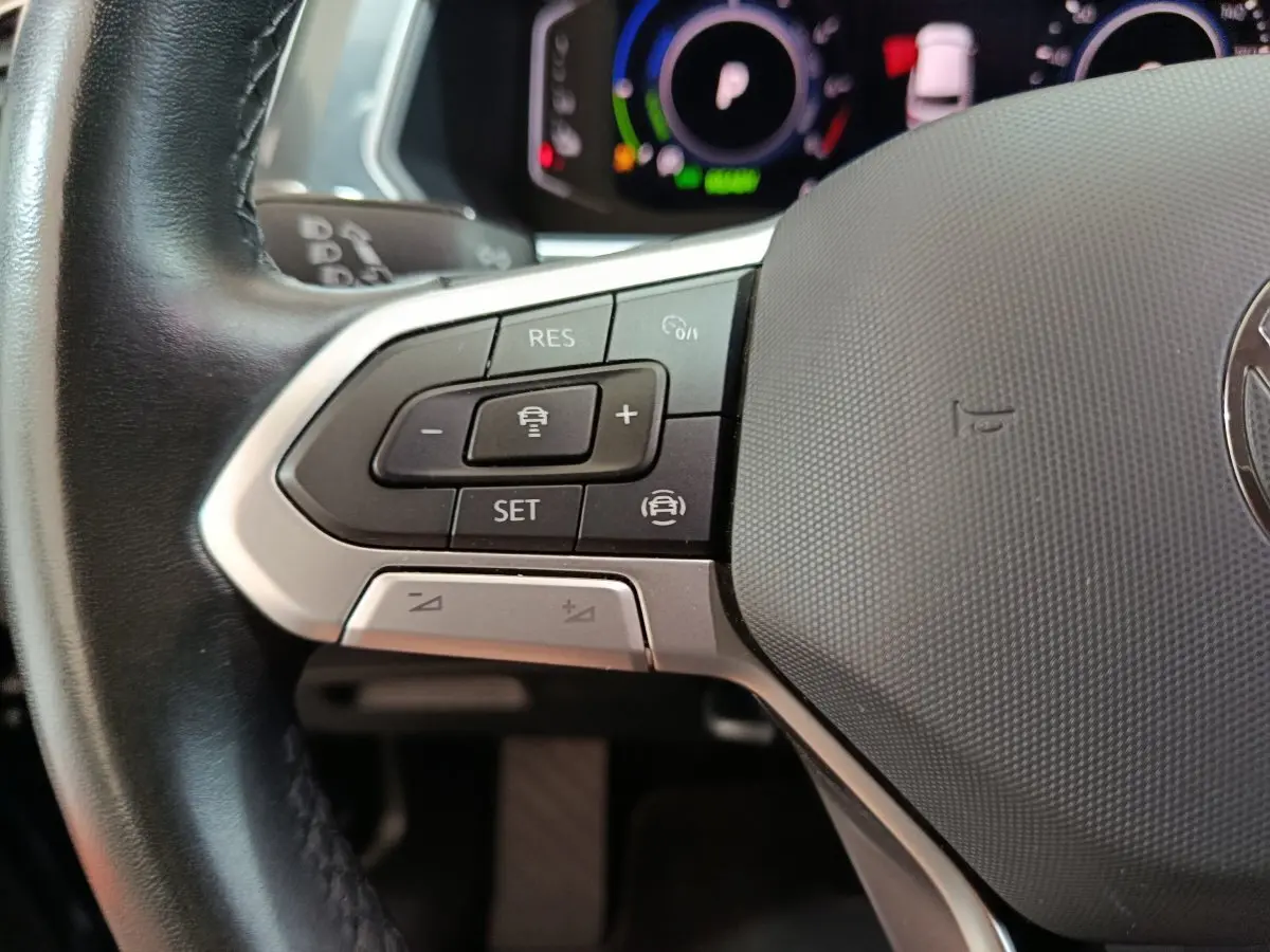 Gros plan sur les commandes gauche du volant cuir du Volkswagen Tiguan hybride rechargeable 2022, affichage numérique en arrière-plan.