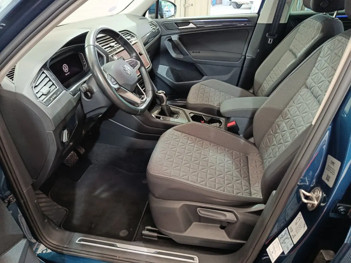 Intérieur côté conducteur du Volkswagen Tiguan bleu 2022, sièges gris à motifs et tableau de bord moderne avec écran tactile.
