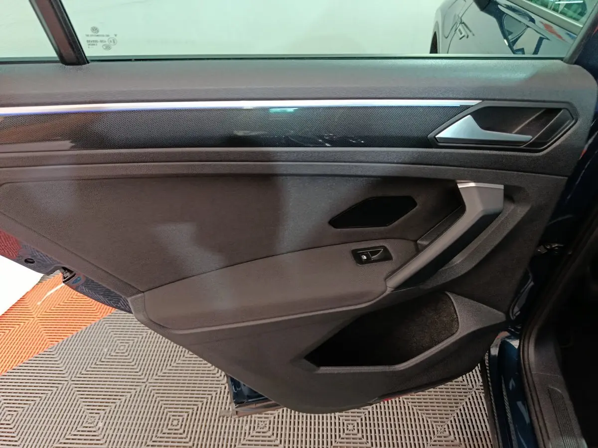 Porte intérieure côté gauche du Volkswagen Tiguan bleu 2022, avec habillage noir et insert décoratif brillant.