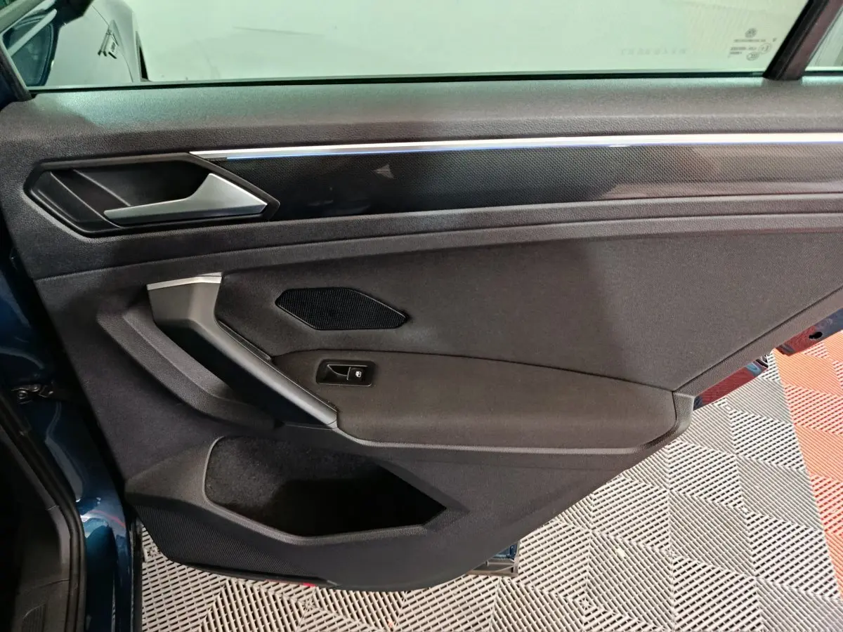Vue côté gauche de la porte intérieure noire du Volkswagen Tiguan bleu avec poignée argentée et haut-parleur intégré.