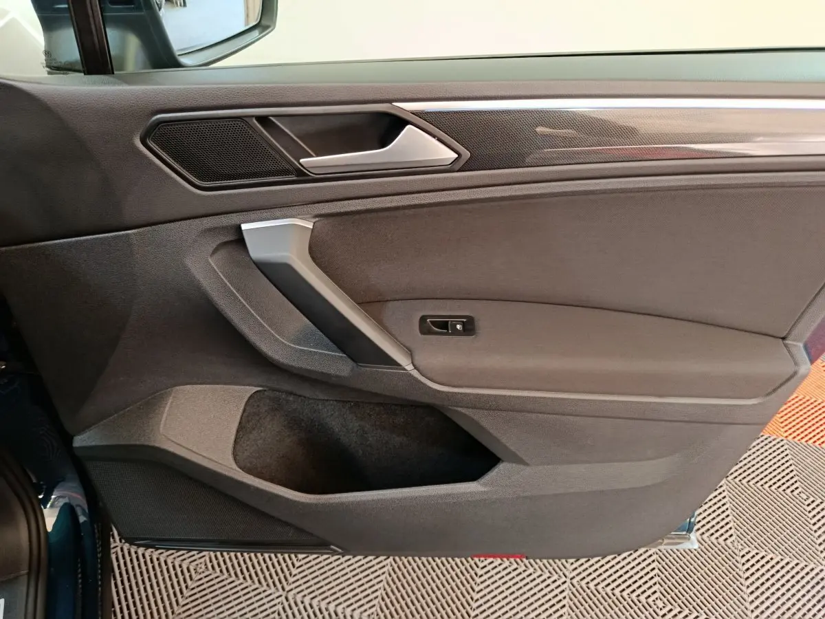 Intérieur côté gauche de la porte du Volkswagen Tiguan bleu 2022, avec poignée argentée et garniture noire.