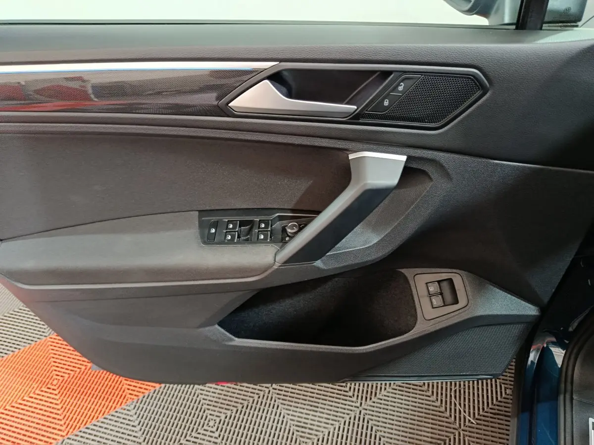 Vue du panneau de porte côté conducteur du Volkswagen Tiguan bleu 2022 avec commandes électriques et finition noire.