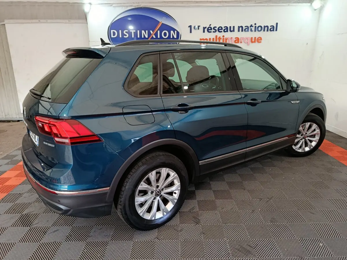 Vue 3/4 arrière droite d'un Volkswagen Tiguan bleu hybride rechargeable avec jantes argentées en intérieur showroom.