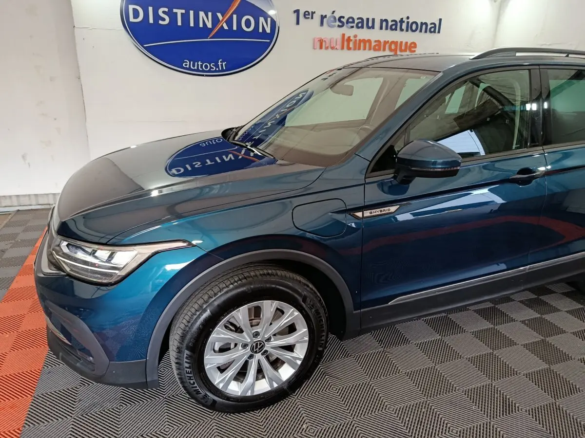 Vue 3/4 avant gauche du Volkswagen Tiguan bleu hybride rechargeable avec badge "eHybrid" sur l'aile avant.