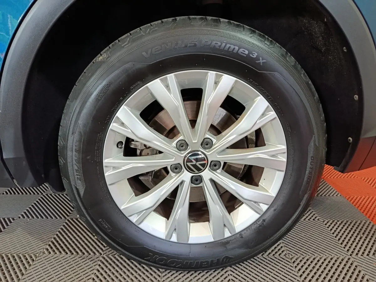 Gros plan sur la roue avant gauche du Volkswagen Tiguan bleu 1.4 eHybrid avec jante en alliage argentée.