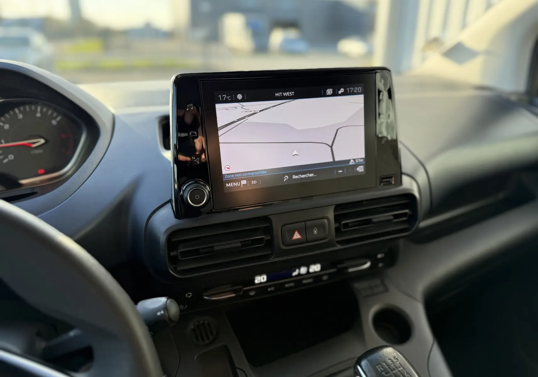 Vue intérieure du tableau de bord du Peugeot Rifter gris platinium, avec écran tactile central affichant la navigation et levier de vitesse manuel visible.
