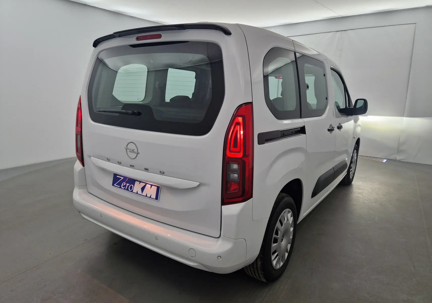 Vue 3/4 arrière droite d'un Opel Combo Life blanc avec feux arrière allumés et becquet noir sur toit.