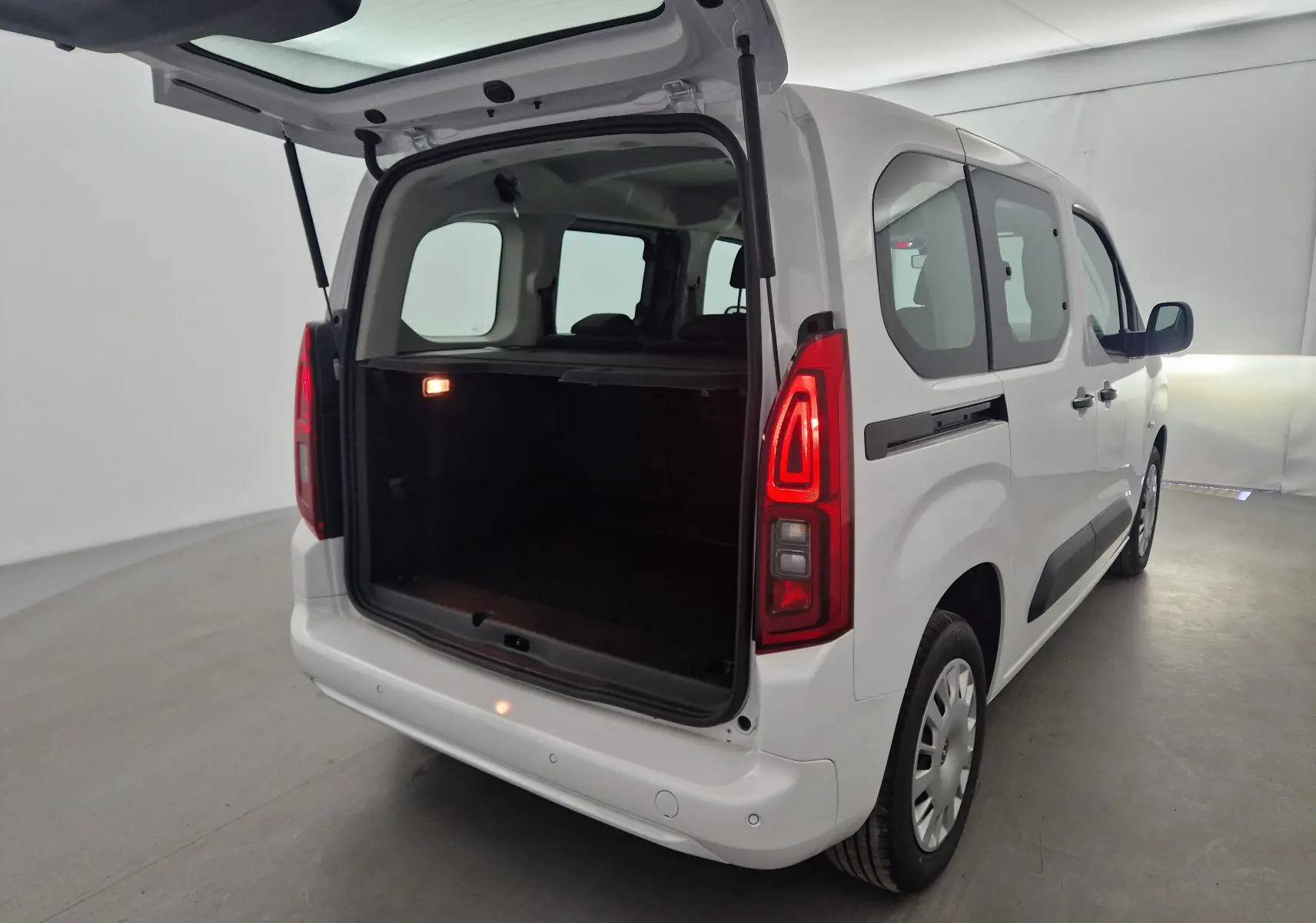Vue 3/4 arrière droite d'un Opel Combo Life blanc avec hayon ouvert et feux arrière allumés dans un studio.