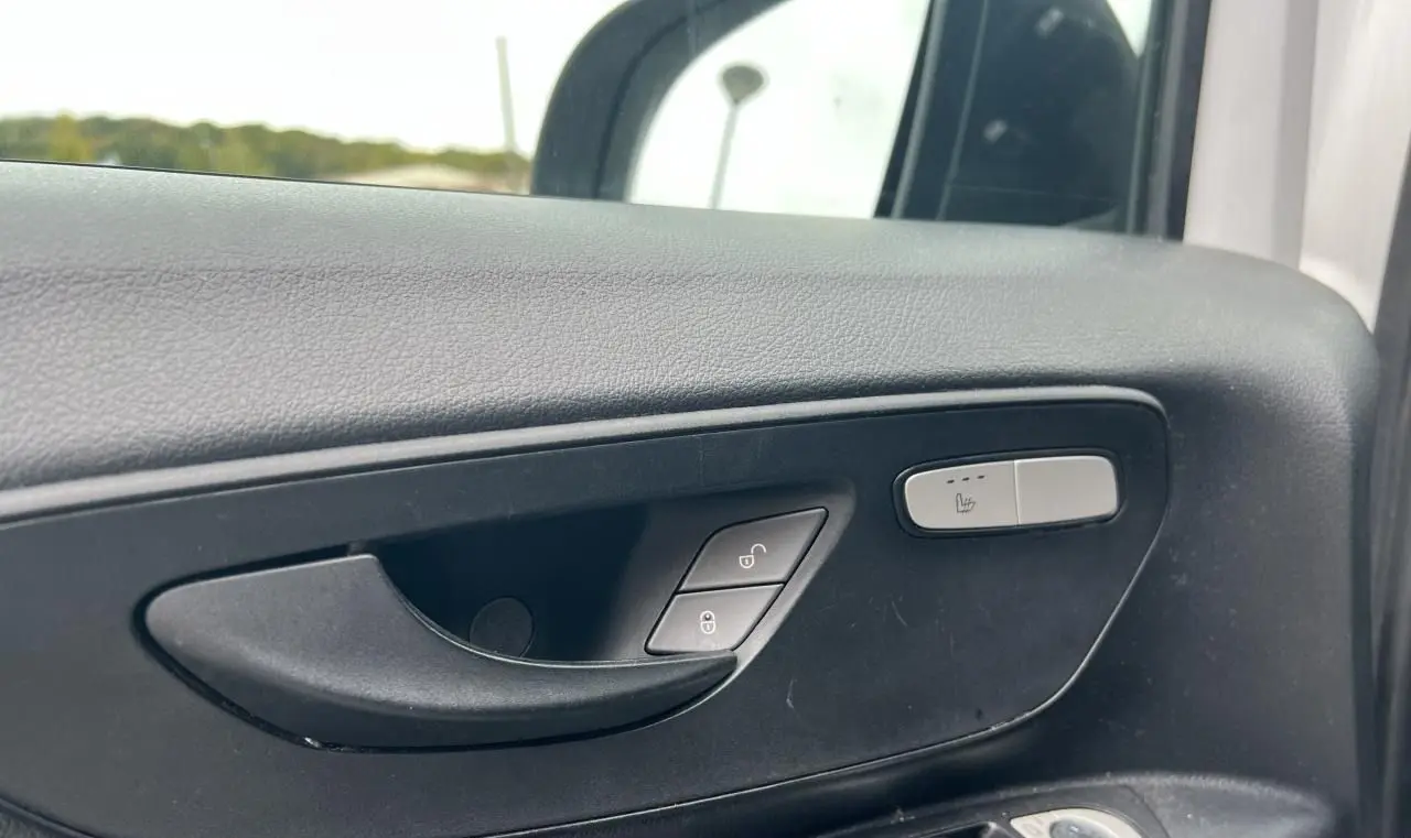 Gros plan sur la poignée intérieure côté gauche du Mercedes Vito Fourgon blanc avec bouton de siège chauffant visible.