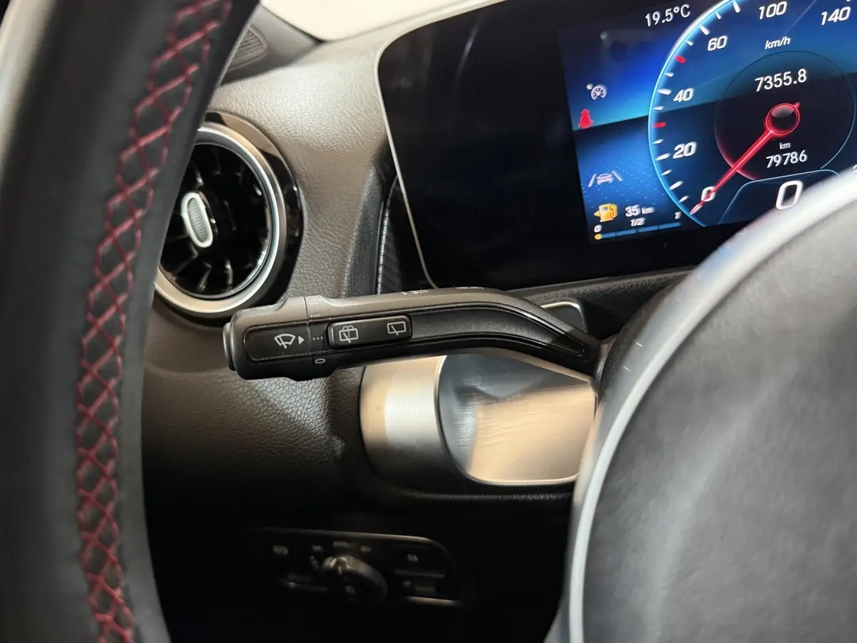 Gros plan sur le commodo de l’essuie-glace et le tableau de bord numérique bleu du Mercedes GLB 200 d AMG Line noir.