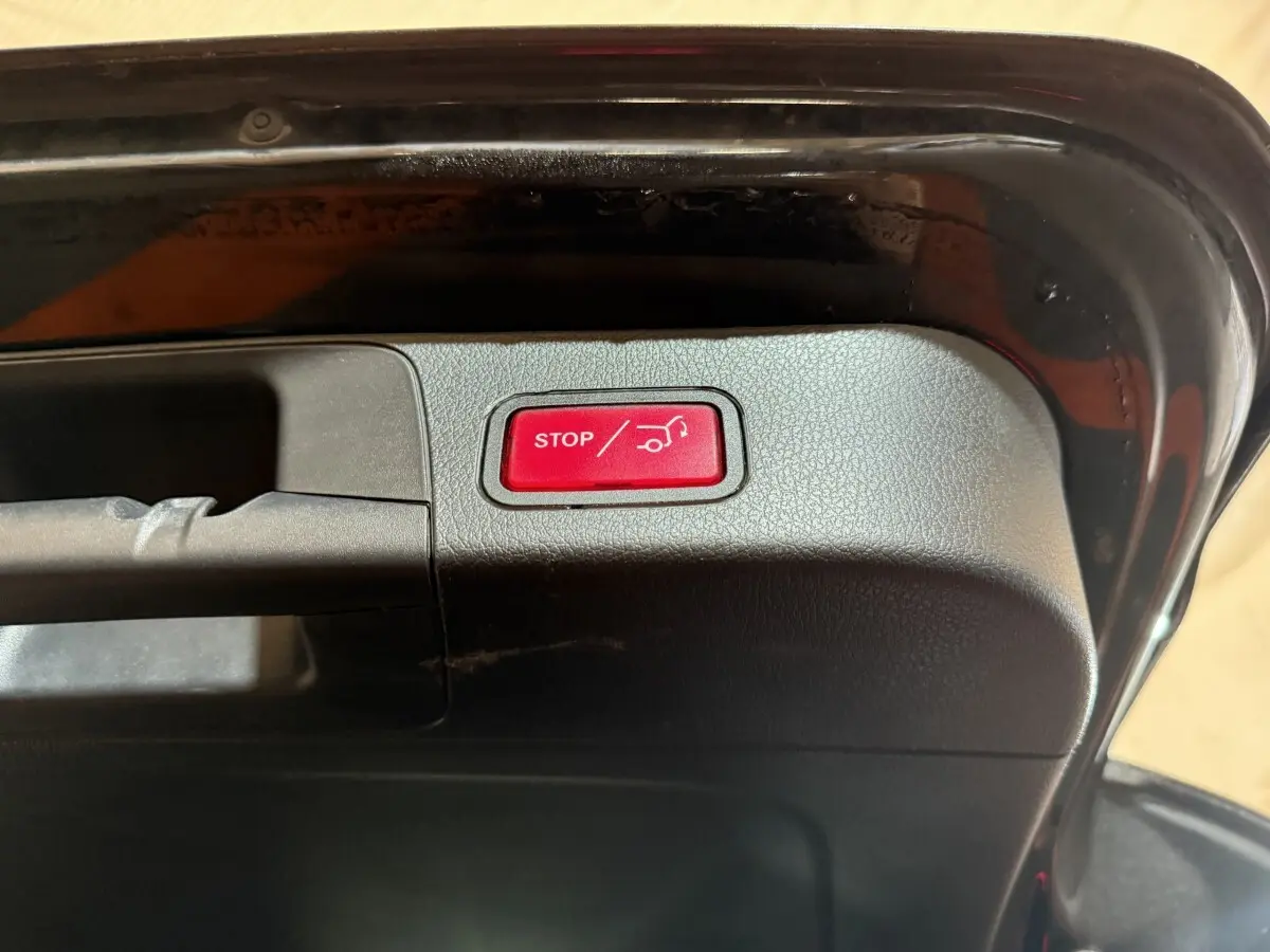 Gros plan sur le bouton rouge stop ouverture/fermeture coffre du Mercedes GLB 200 d AMG Line noir, vue intérieure du hayon ouvert.