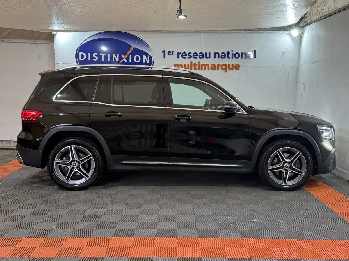 Profil côté gauche d'un Mercedes GLB 200 d AMG Line noir, avec jantes alliage et rails de toit chromés en intérieur showroom.