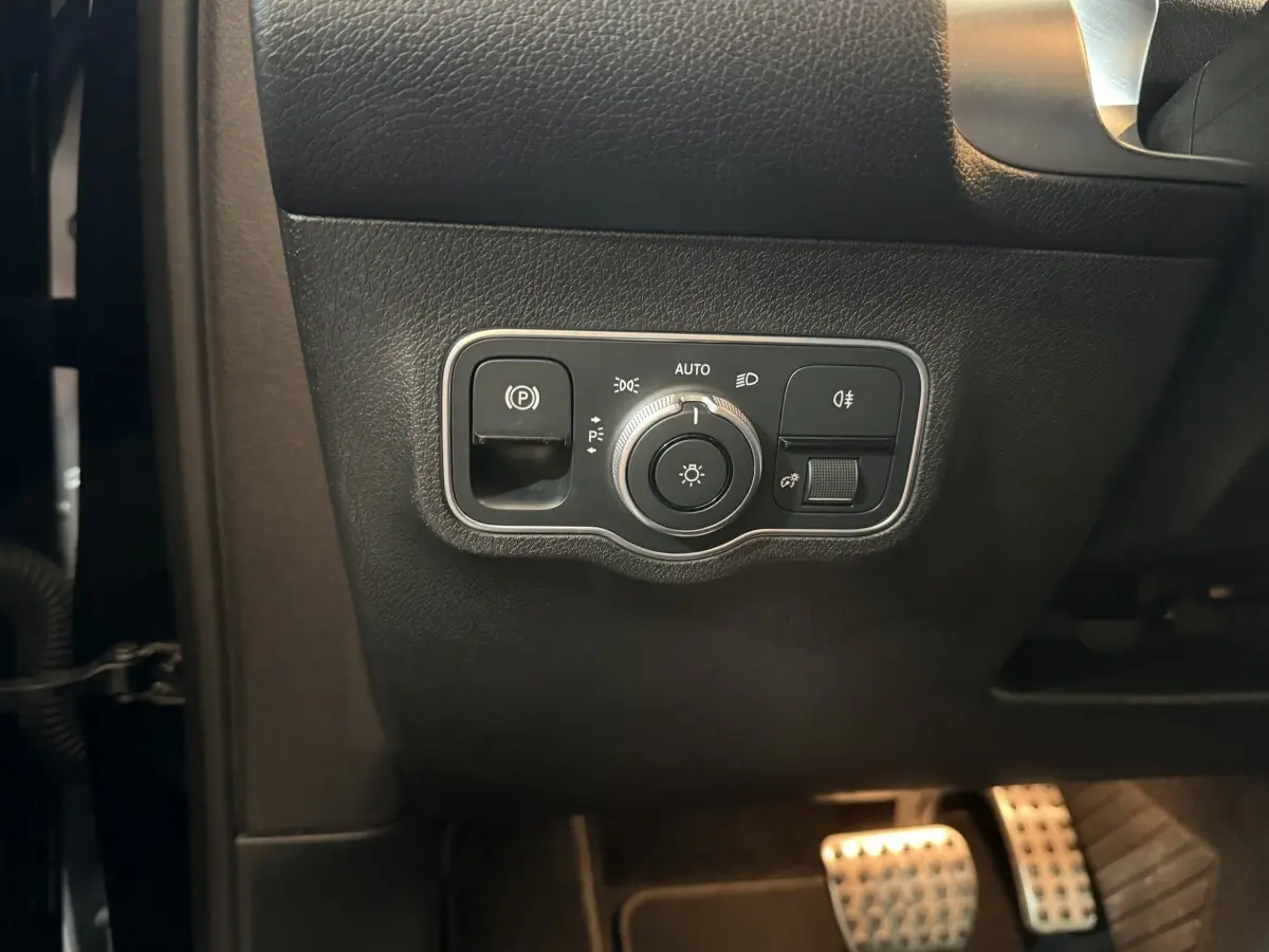 Gros plan sur les commandes d’éclairage et frein à main électrique côté gauche du tableau de bord noir du Mercedes GLB 200 d AMG Line 2020.