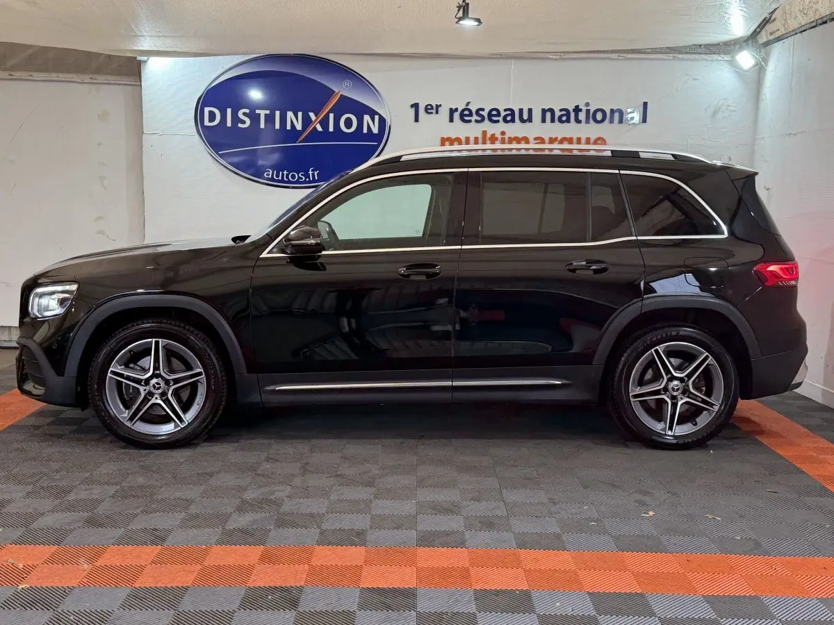 Profil côté gauche d'un Mercedes GLB 200 d AMG Line noir avec jantes alliage et barres de toit chromées en intérieur showroom.