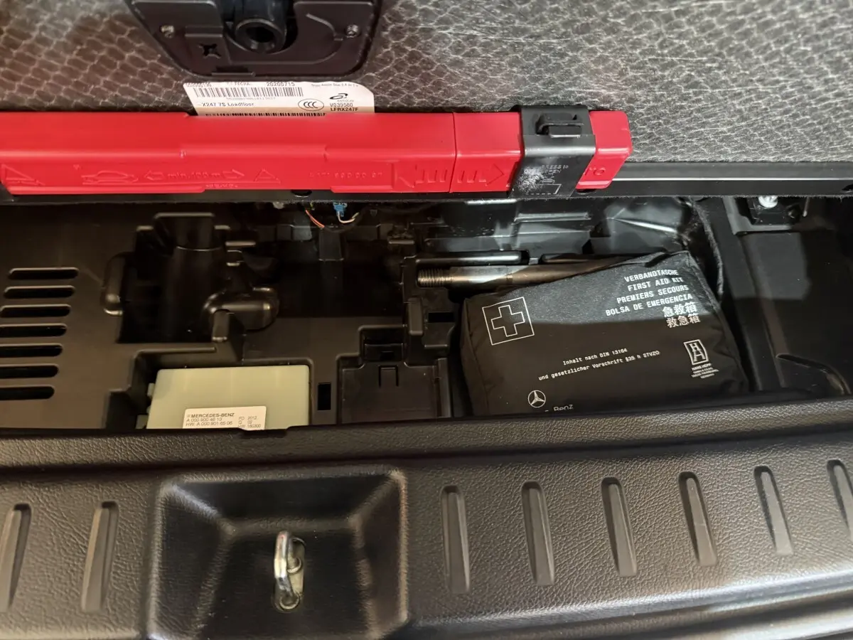 Vue rapprochée du coffre du Mercedes GLB 200 d AMG Line noir, montrant la trousse de premiers secours et le triangle de signalisation.