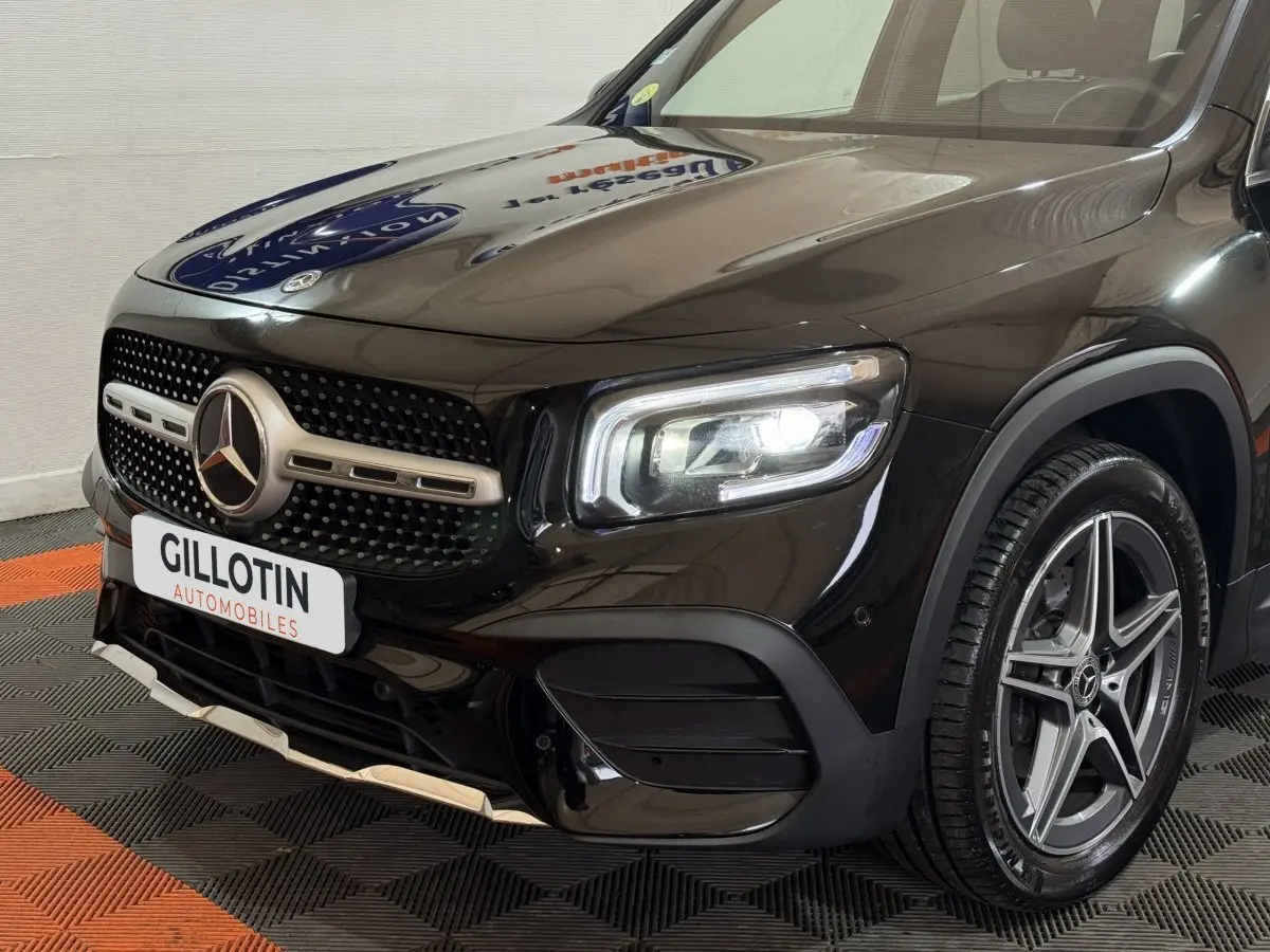 Vue 3/4 avant droit du Mercedes GLB 200 d AMG Line noir avec calandre étoilée et phares LED allumés.
