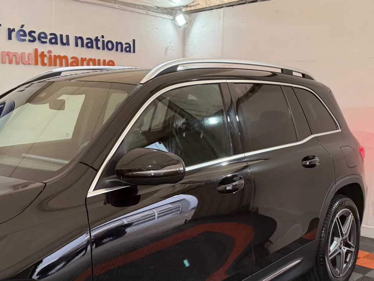 Vue latérale côté gauche d'un Mercedes GLB 200 d AMG Line noir avec barres de toit chromées et jantes alliage cinq branches.