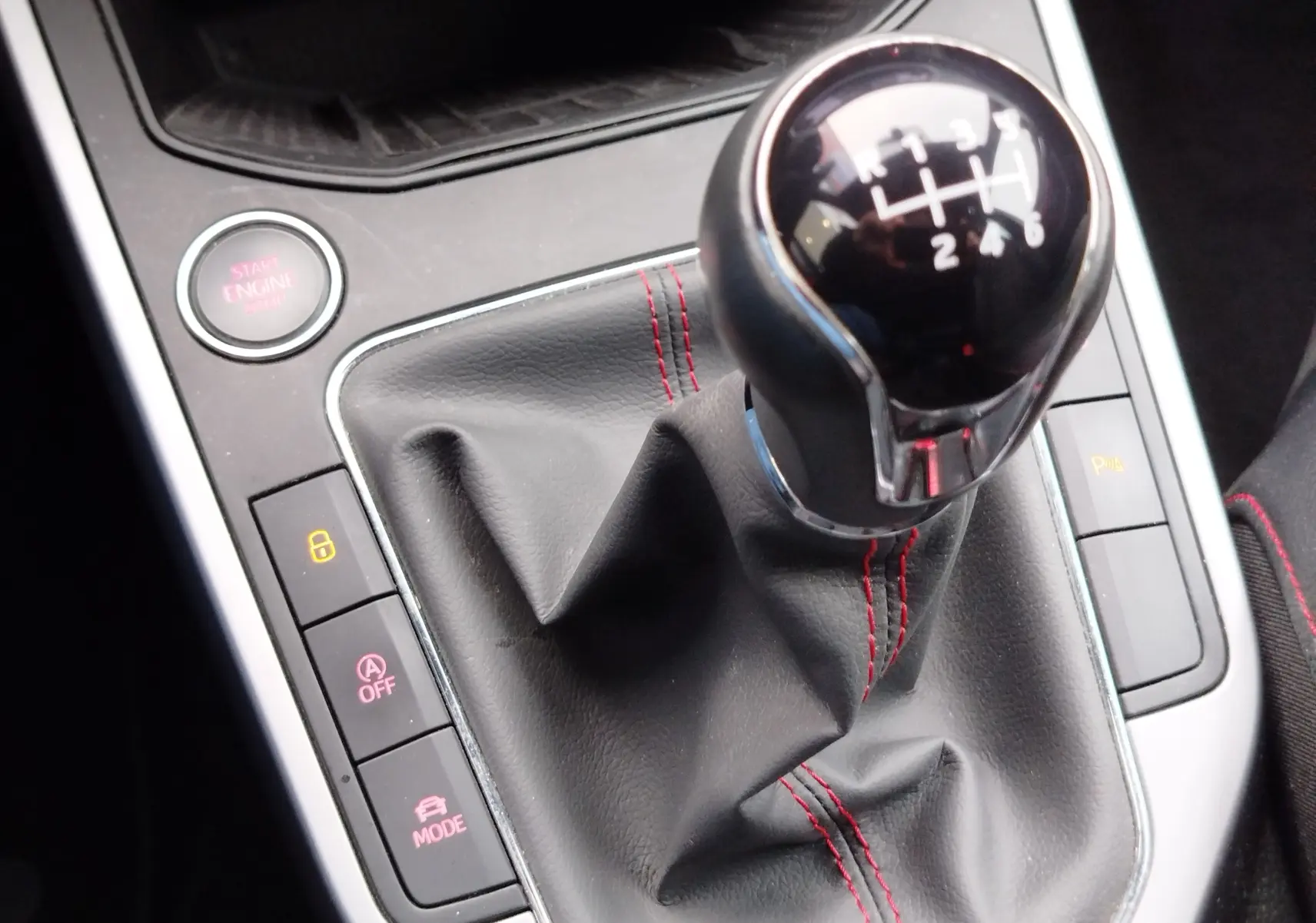 Gros plan sur le levier de vitesses manuel avec surpiqûres rouges et bouton start/stop dans l’habitacle du SEAT Arona.