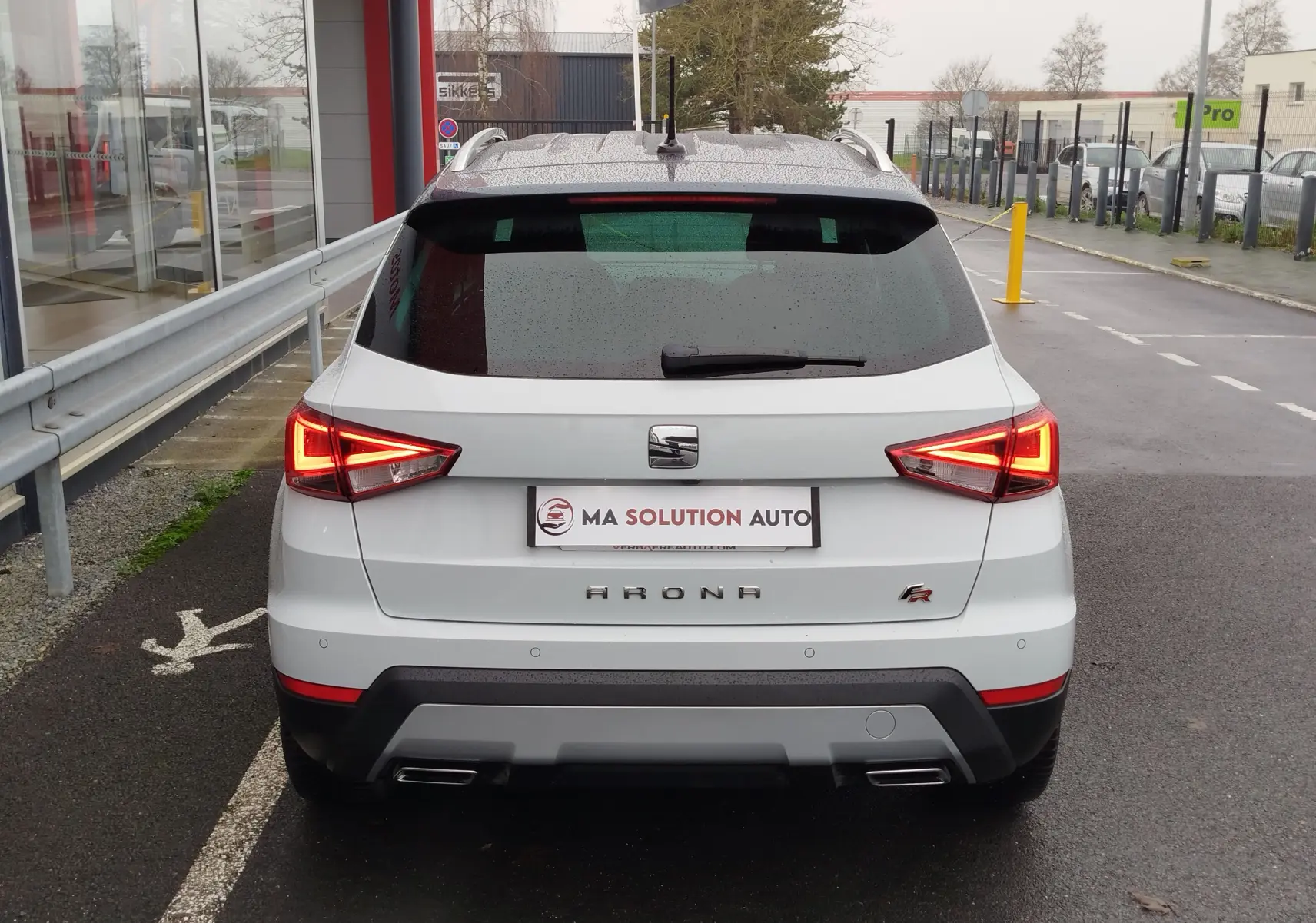 Vue arrière d'un SEAT Arona blanc avec toit gris magnétique, feux arrière allumés et double sortie d'échappement.