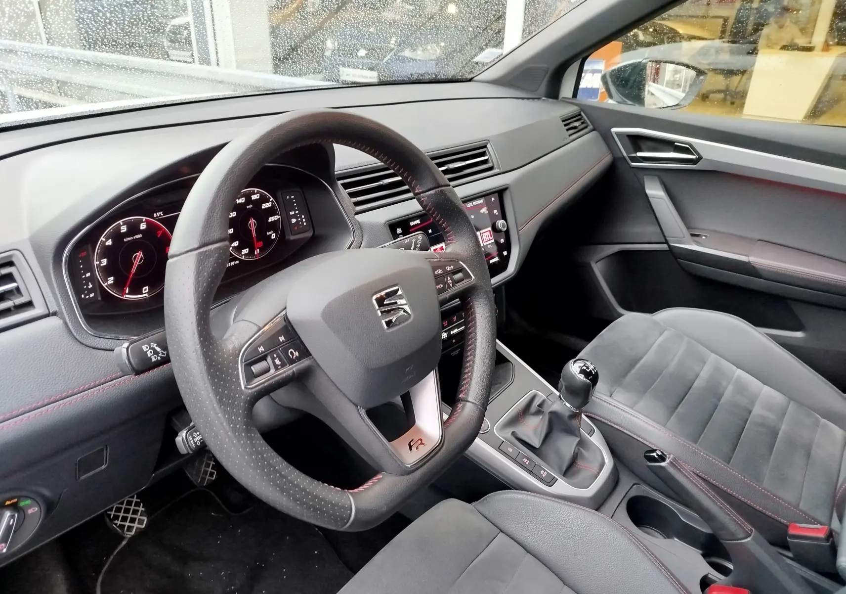 Vue intérieure côté conducteur du SEAT Arona 2020, volant cuir perforé avec surpiqûres rouges et levier de vitesses manuel.