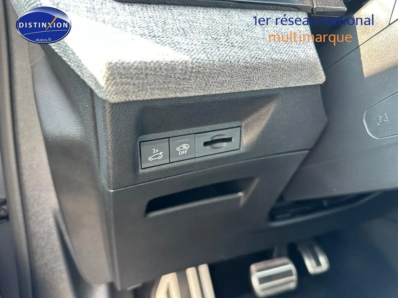 Gros plan sur la partie inférieure gauche du tableau de bord gris avec commandes d'ouverture du coffre et pédalier sport en aluminium.