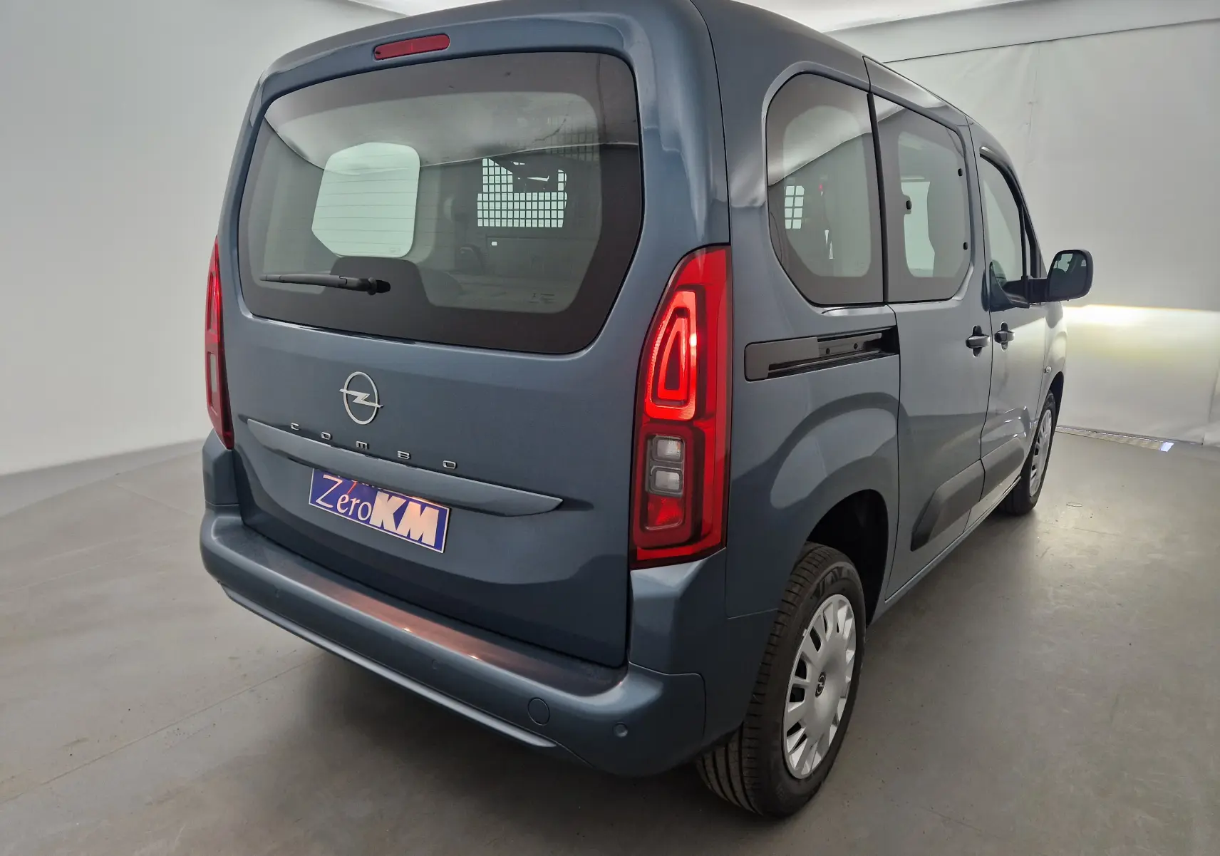 Vue 3/4 arrière droite d'un Opel Combo Life bleu Kiama avec feux allumés et grille de séparation visible à l'intérieur.