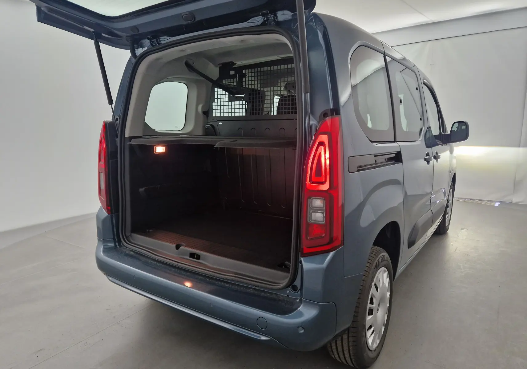 Vue 3/4 arrière droite d'un Opel Combo Life bleu Kiama avec coffre ouvert et grille de séparation visible.
