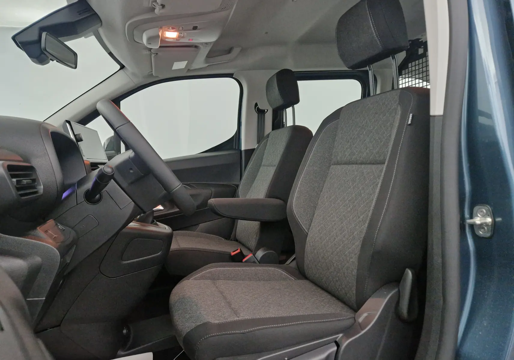 Vue intérieure côté conducteur de l'Opel Combo Life bleu Kiama, sièges tissu gris avec accoudoir et grille de séparation.