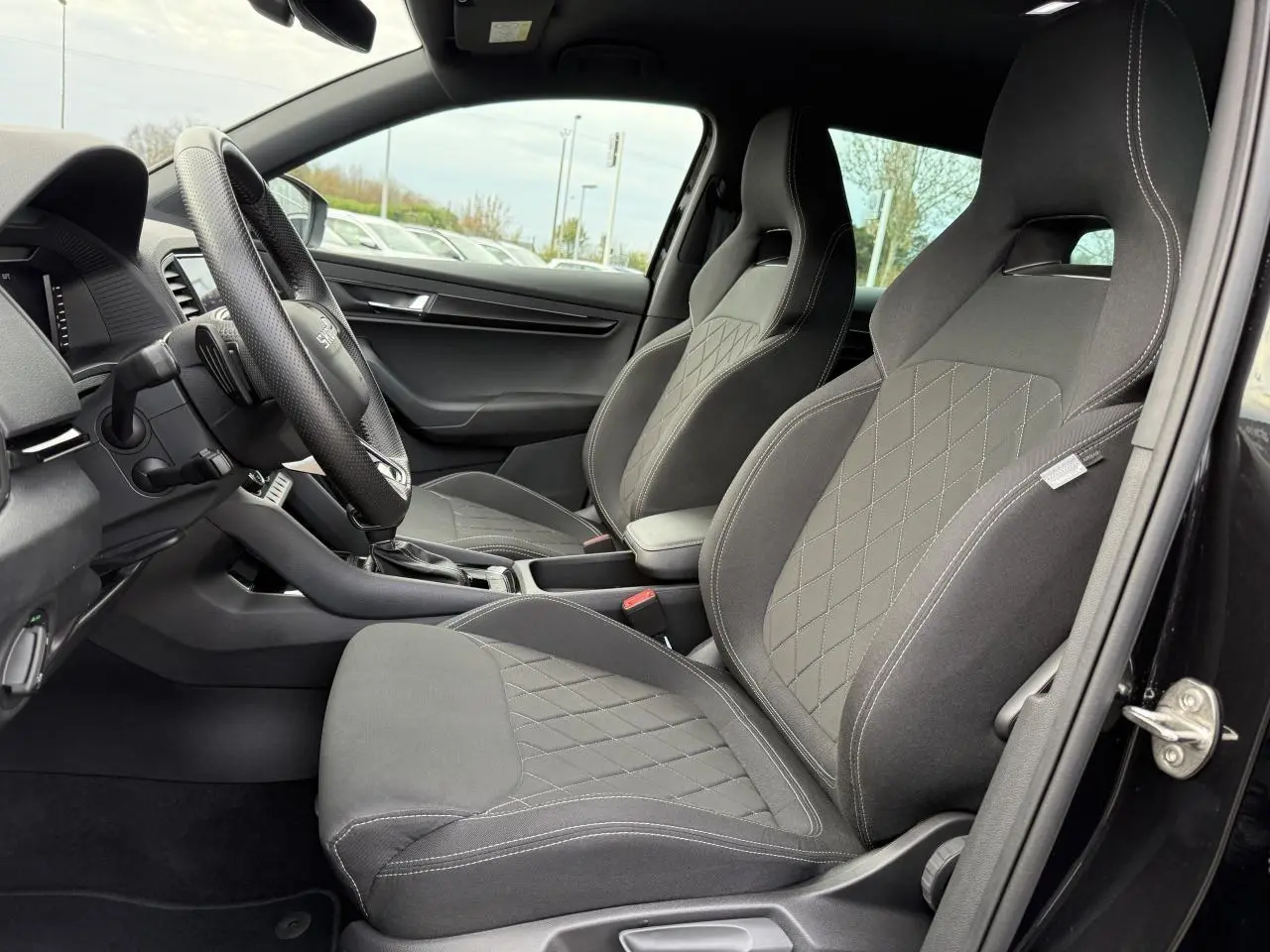 Vue intérieure côté conducteur du Skoda Karoq noir Magic nacré, mettant en valeur les sièges sport en tissu noir avec surpiqûres contrastées.