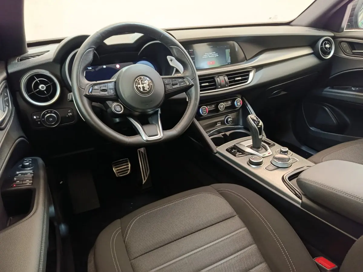 Intérieur noir de l'Alfa Romeo Stelvio 2024, vue côté conducteur sur volant, tableau de bord et console centrale.