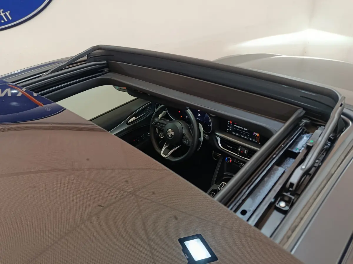 Vue plongeante sur l'intérieur noir d'un Alfa Romeo Stelvio gris foncé 2024, tableau de bord et volant visibles via toit ouvrant.