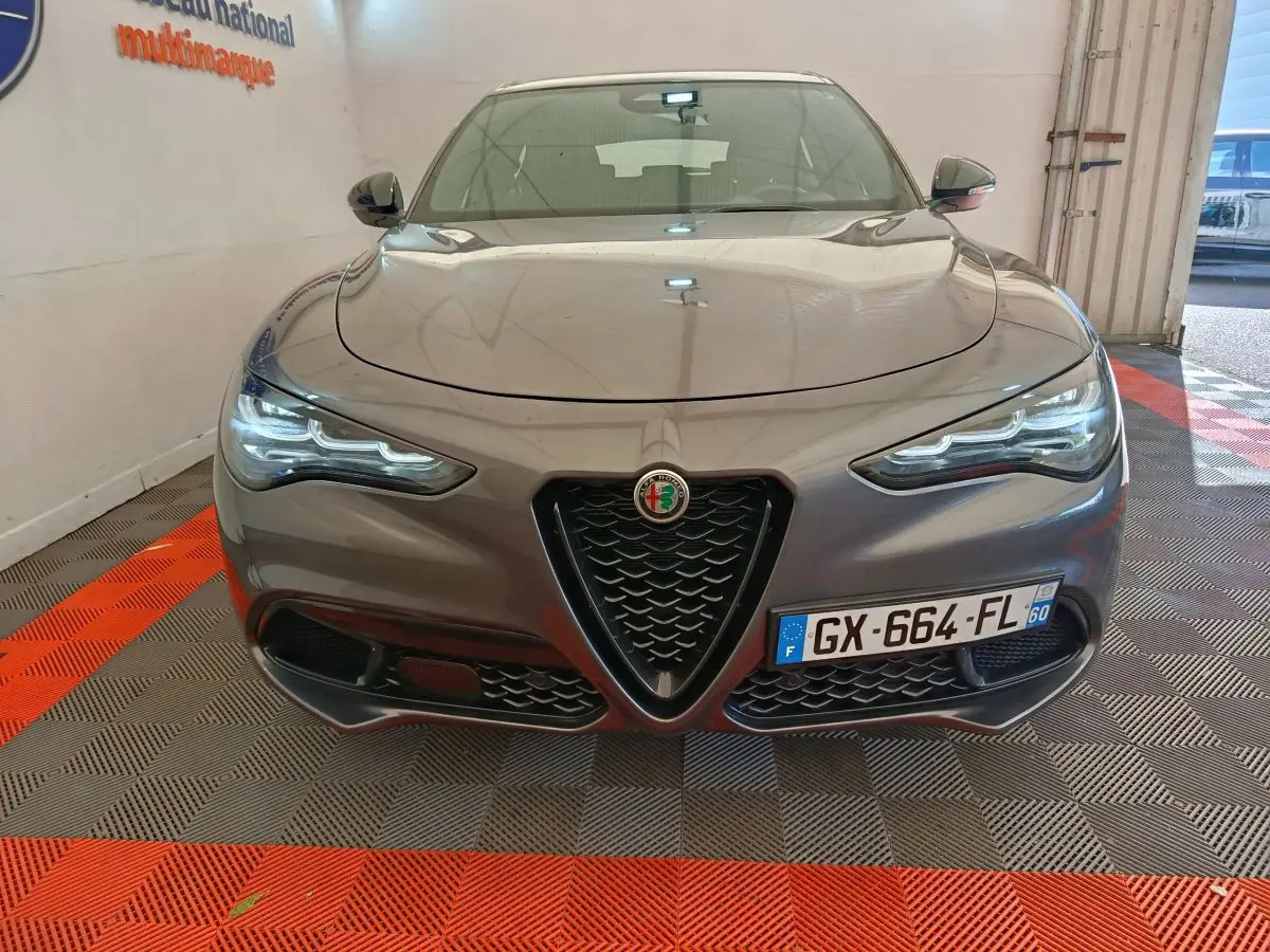 Vue frontale d'un Alfa Romeo Stelvio gris foncé avec calandre triangulaire et phares LED allumés.
