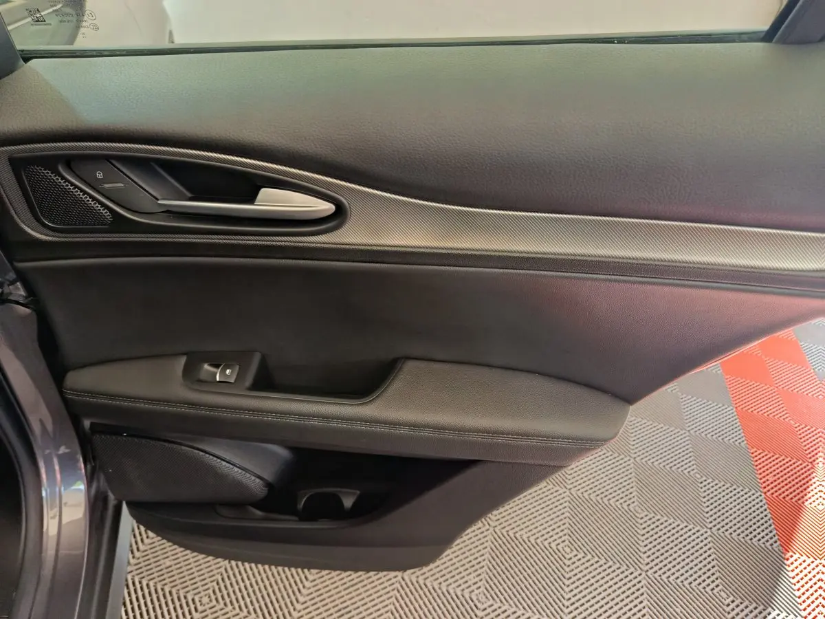Détail de la porte côté gauche de l'Alfa Romeo Stelvio gris foncé 2024 avec poignée argentée et garniture noire.