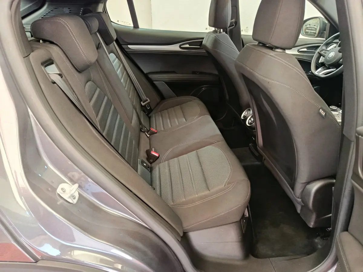 Vue côté gauche arrière de l'habitacle gris foncé de l'Alfa Romeo Stelvio avec sièges tissu et détails intérieurs visibles.