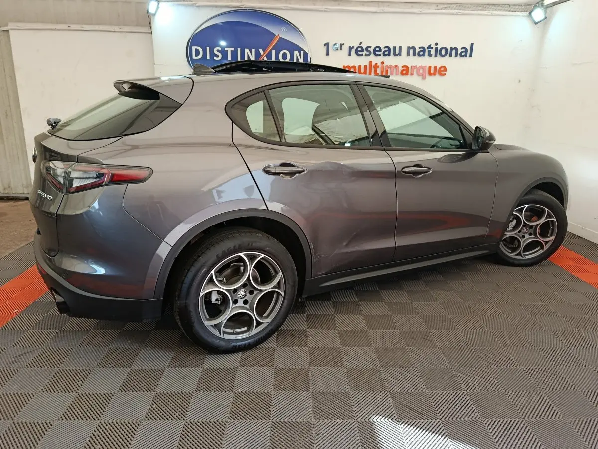 Vue côté gauche d'un Alfa Romeo Stelvio gris foncé 2024 avec jantes spécifiques et feux arrière LED dans un showroom.