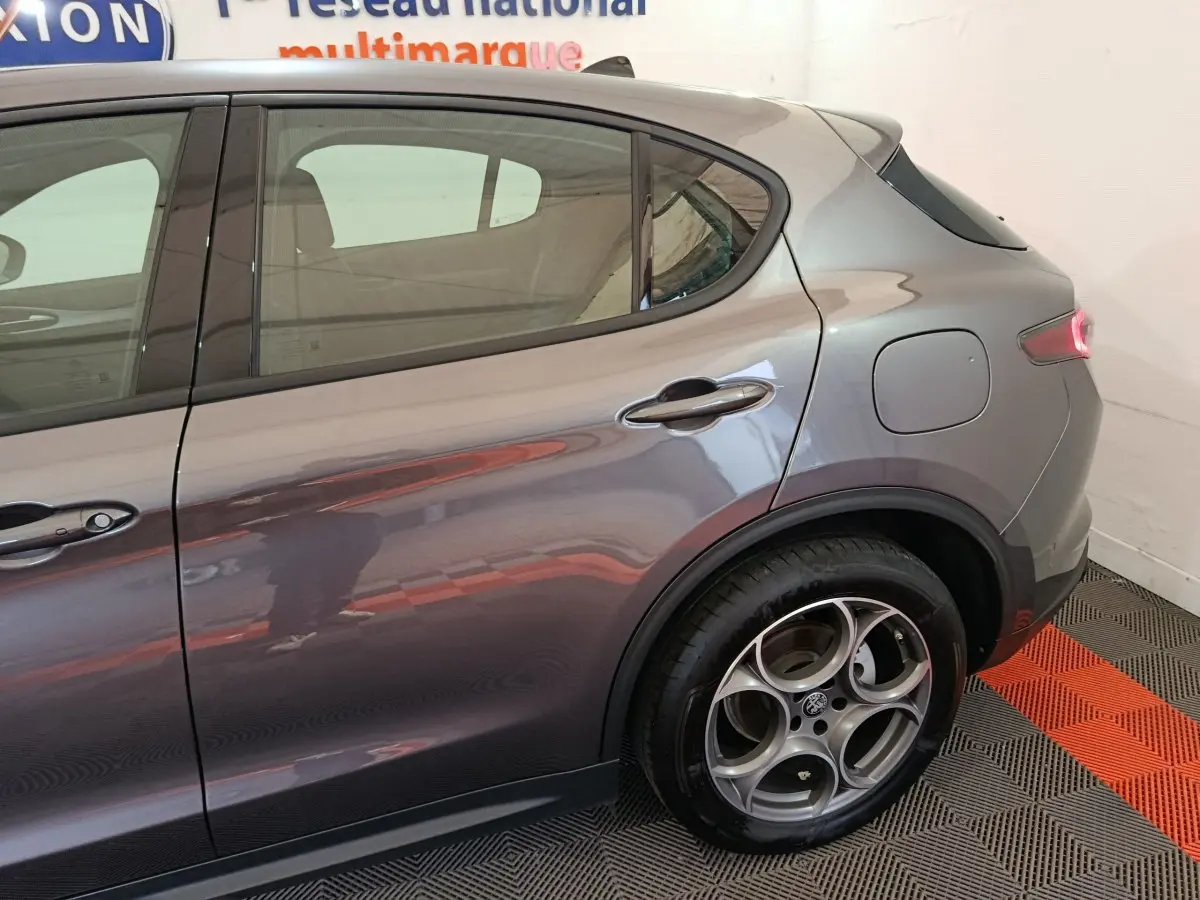 Vue latérale droite sur l'arrière d'un Alfa Romeo Stelvio gris foncé avec jante alu distinctive à cinq cercles.