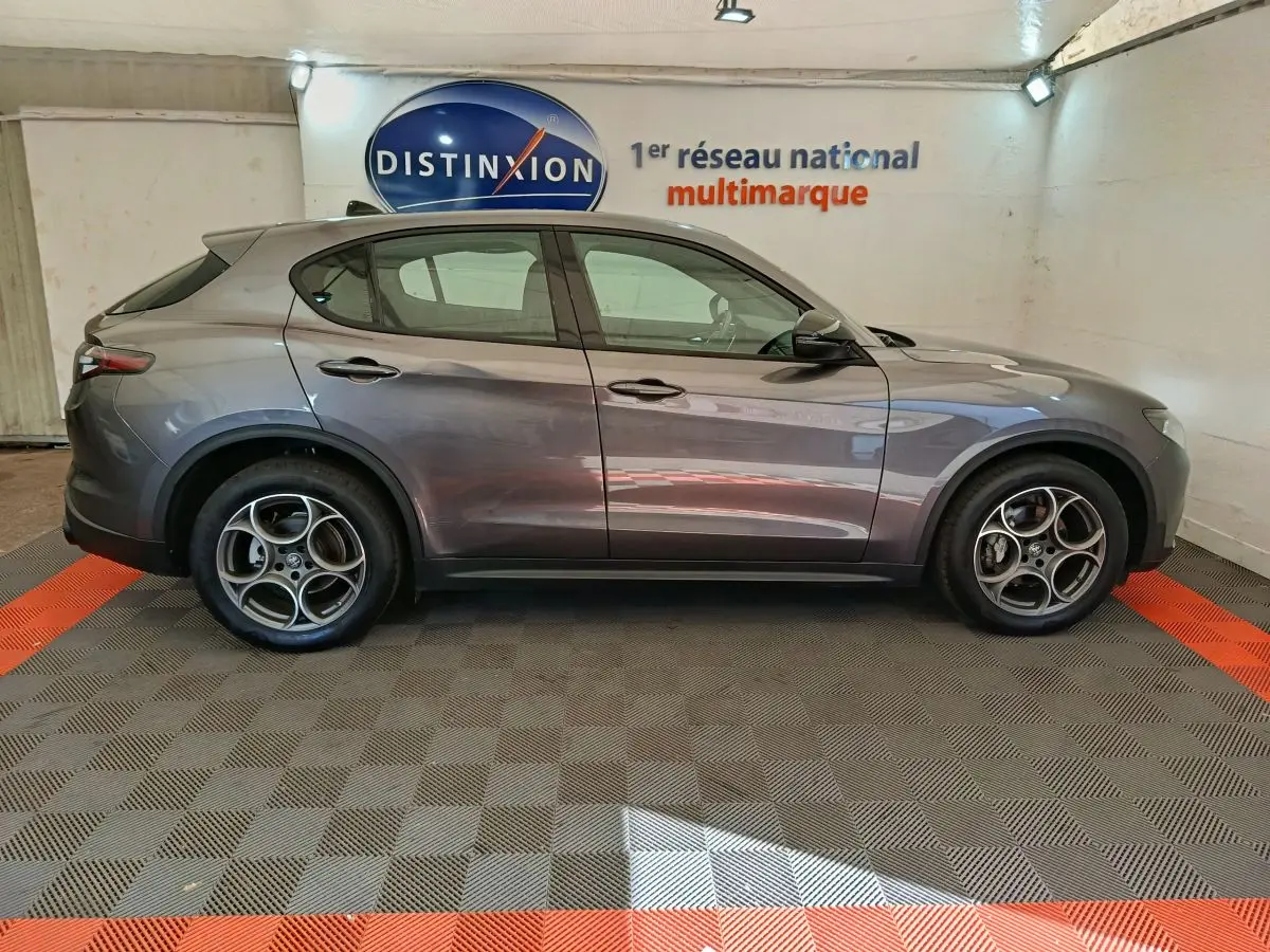 Vue de profil côté gauche d'un Alfa Romeo Stelvio gris foncé 2024 dans un showroom multimarque.