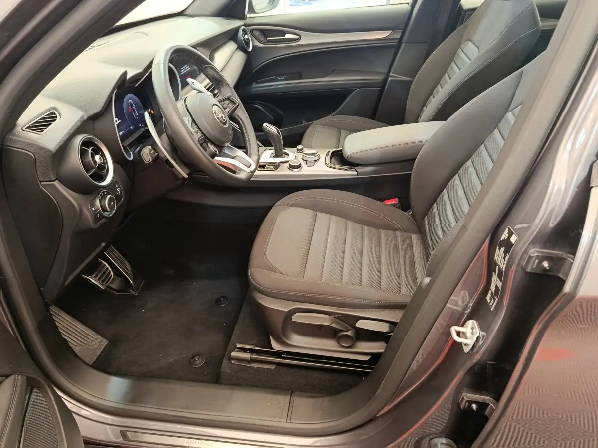 Vue intérieure côté conducteur de l'Alfa Romeo Stelvio gris foncé, avec sièges tissu et tableau de bord moderne.