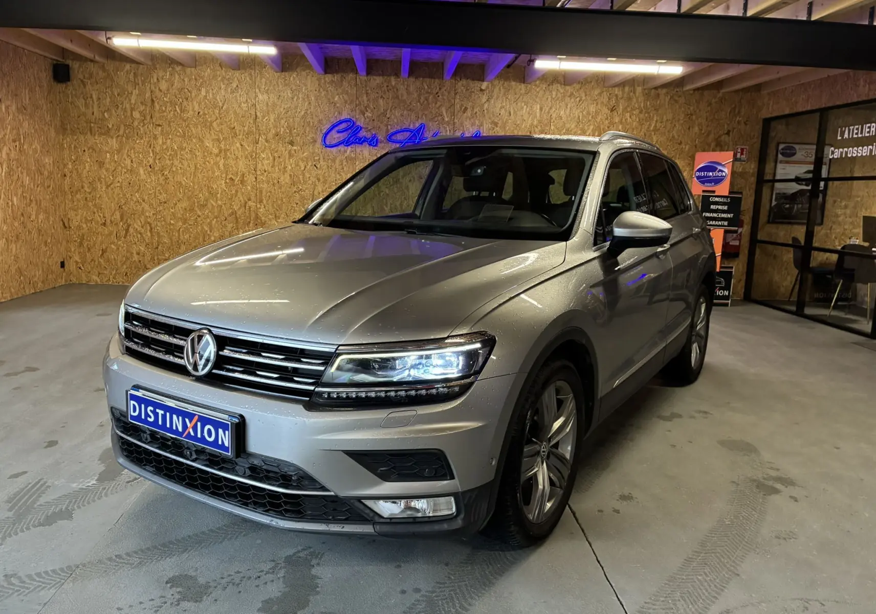 Vue 3/4 avant d'un Volkswagen Tiguan gris 2017 avec phares allumés dans un garage au sol béton.
