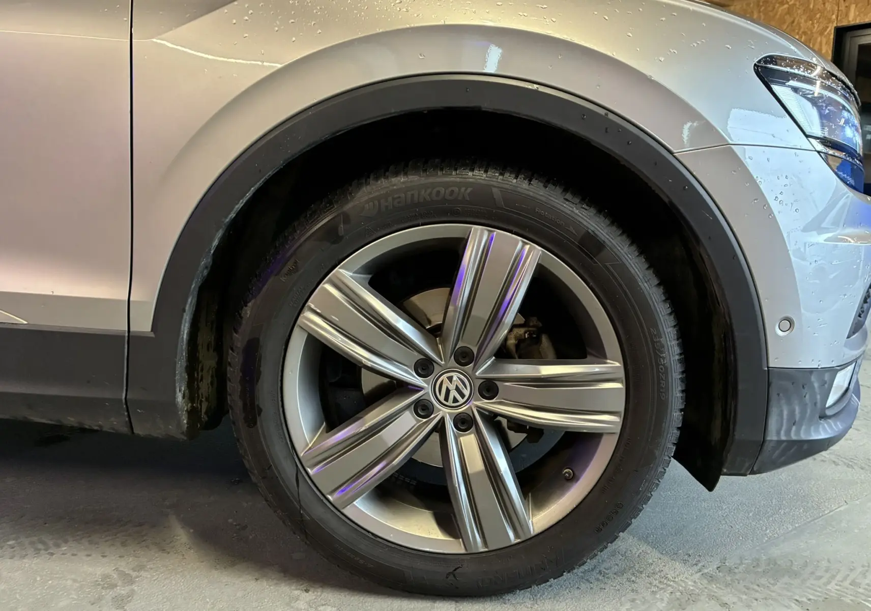 Gros plan sur la roue avant droite d’un Volkswagen Tiguan gris 2017 avec jante alliage 5 branches et logo VW central.