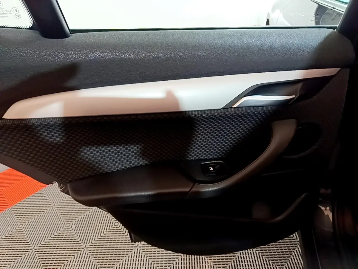 Vue intérieure du panneau de porte côté droit de BMW X2 gris foncé, avec poignée argentée et bouton de verrouillage.