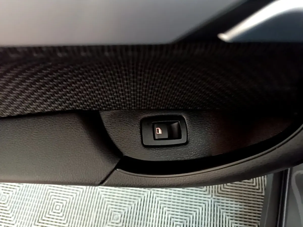 Gros plan sur le bouton d'ouverture électrique du coffre dans l'habitacle d'une BMW X2 gris foncé.