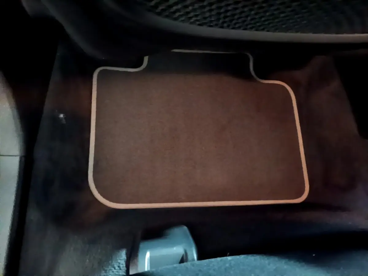 Tapis de sol beige sur fond noir, vue rapprochée de l'intérieur côté passager d'une BMW X2 gris foncé.