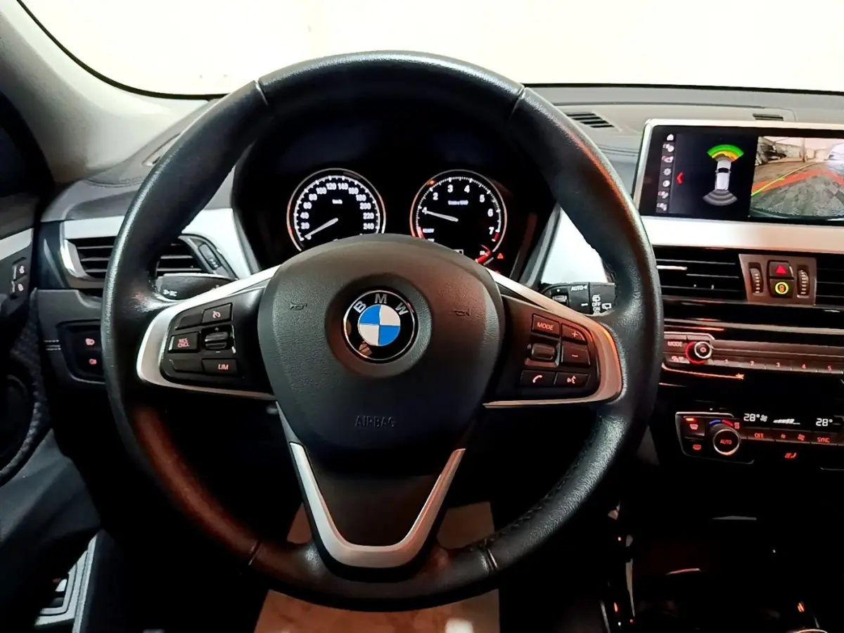 Vue intérieure centrée sur le volant cuir noir de la BMW X2 2021 avec tableau de bord et écran multimédia affichant l'aide au stationnement.