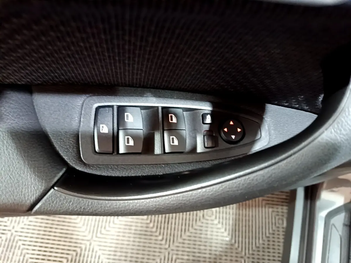 Gros plan sur les commandes des vitres et rétroviseurs côté gauche d’une BMW X2 gris foncé 2021.