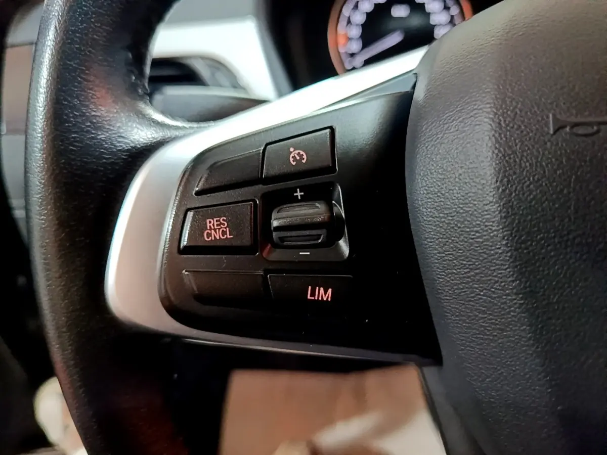 Gros plan sur les commandes du régulateur de vitesse au volant cuir d’une BMW X2 sDrive18i Lounge gris foncé.