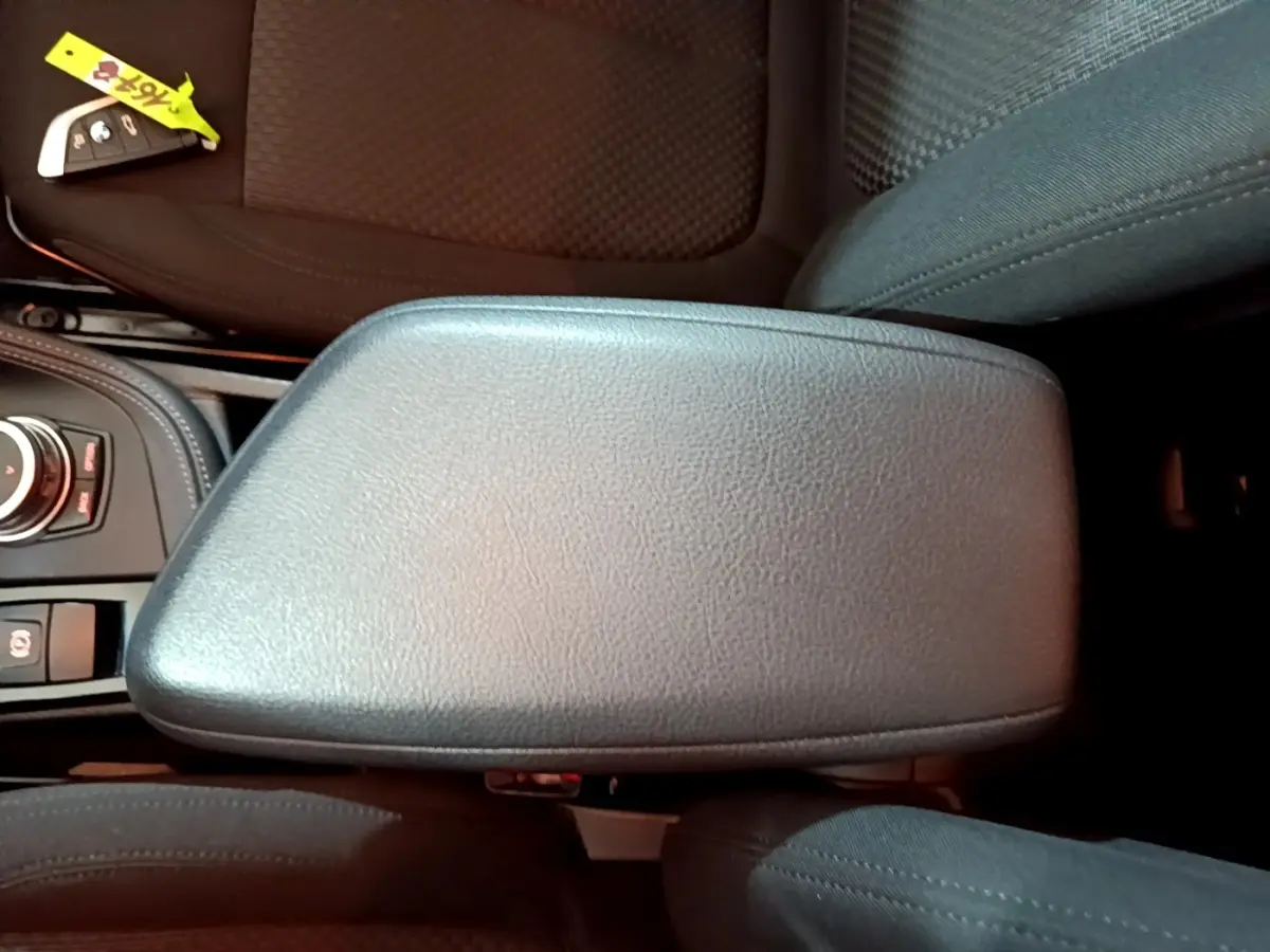 Vue rapprochée de l'accoudoir central en cuir noir et de la clé BMW sur le siège avant d'un BMW X2 gris foncé.