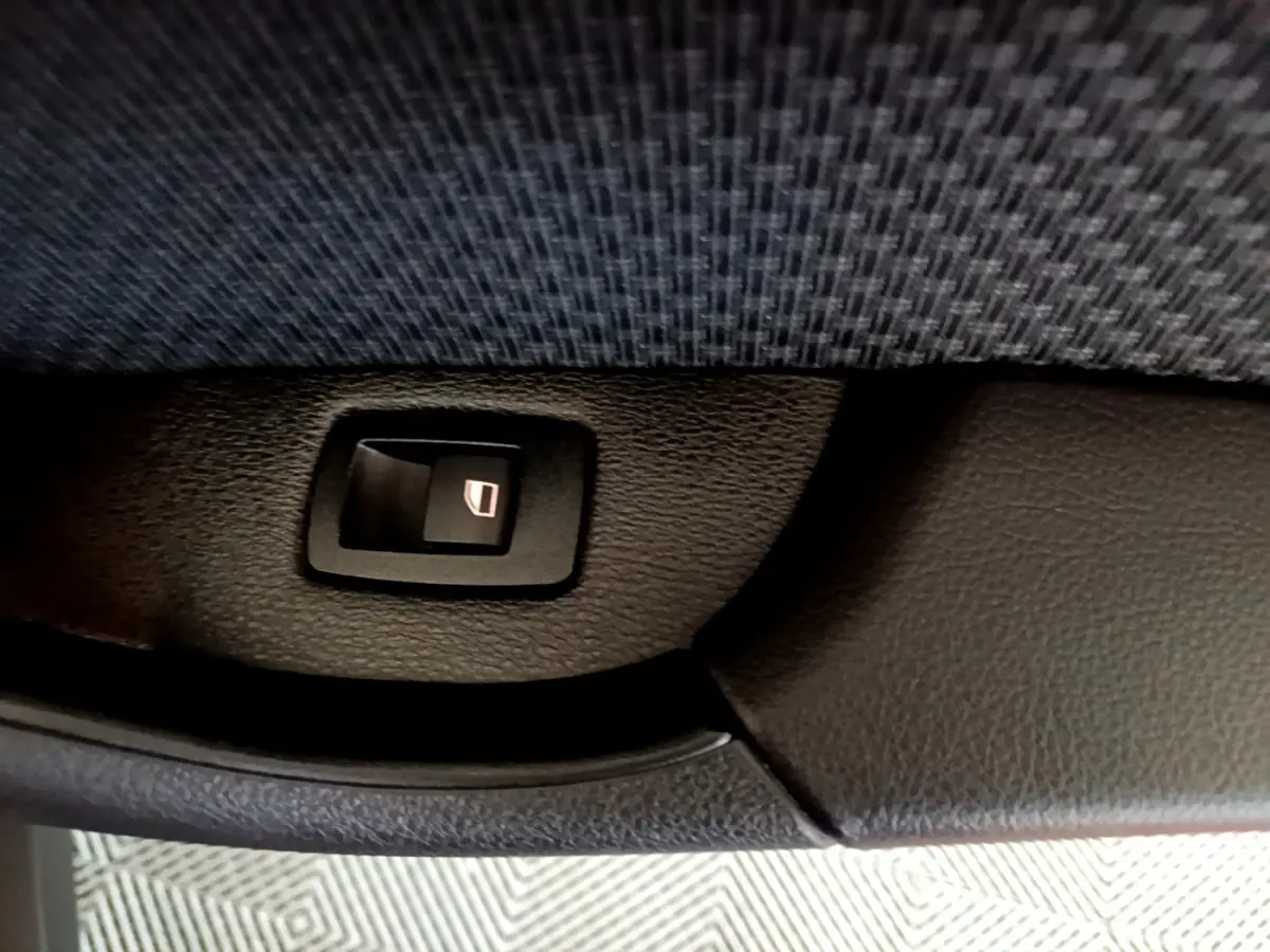 Détail du bouton de commande de lève-vitre sur la porte intérieure d’un BMW X2 gris foncé.